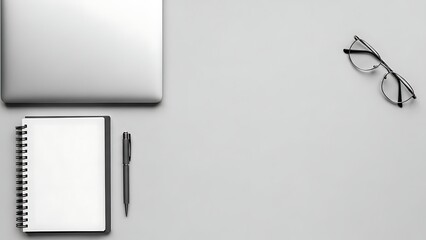 Overhead shot of a minimalist workspace with a laptop, notebook, pen, and eyeglasses on a grey desk.