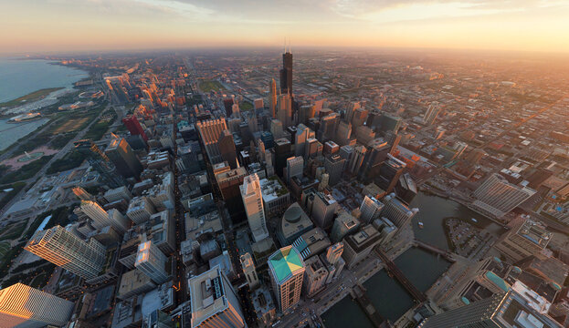 Aerial view of a sprawling cityscape, where the iconic Willis Tower pierces the skyline amidst the warm glow of the setting sun, Chicago, Illinois, United States.
