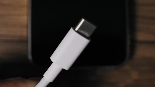Extreme close-up of fingers holding and inspecting the metal tip of a white USB-C cable connector. The detailed macro view highlights the reversible design of modern tech ports.