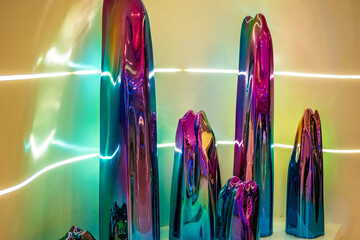 vibrant art pieces are likely contemporary abstract sculptures made of a reflective material with an iridescent finish, illuminated by neon or LED lights