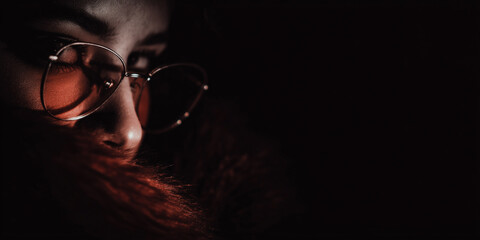 Stylish woman in red tinted glasses in low key lighting, partial face and hair visible, elegant, mysterious fashion portrait with dramatic shadows copy space banner