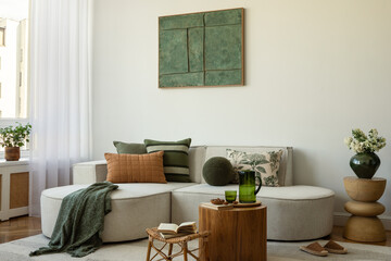 Obraz premium Neutral living room with a sectional sofa, green and brown cushions, wooden coffee tables, and fresh greenery in a ceramic vase.