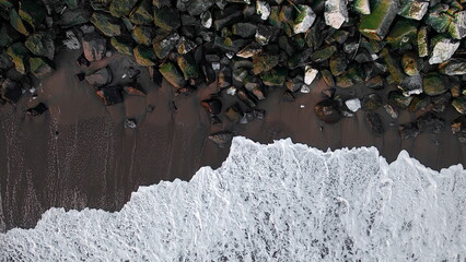 Aerial view of the rhythmic crash of frothy white waves against the dark, rugged rocks of the coastline, Santa Cruz, California, United States.