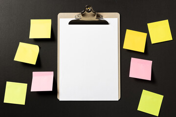 Blank white paper on clipboard with colorful sticky notes on dark background. template mock up