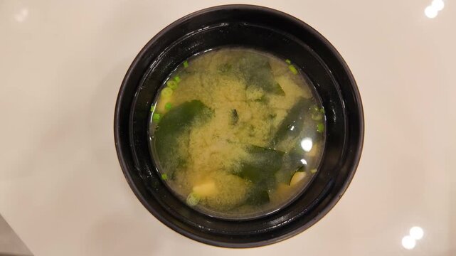 Camera footage of miso soup bowl on white table
