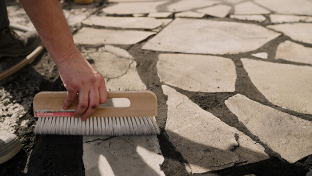 Worker brushing sand into flagstone patio gaps
