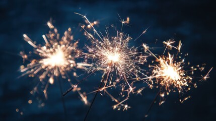 Three handheld sparklers burning with bright golden sparks against a dark background at night