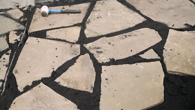 Flagstone patio construction in progress, workers installing natural stone pavers with sand and a rubber mallet
