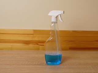 Plastic spray bottle with blue liquid standing on a wooden table surface.
