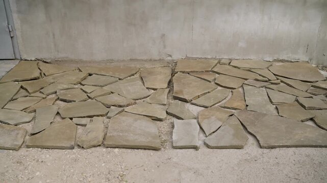 Sandstone flagstone pieces creating a mosaic pattern on a concrete floor, ready for grouting. Construction and renovation process