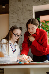 Fototapeta premium Two students work together on a craft project, surrounded by art supplies in a warm, inviting space. Their focus and excitement reflect the joy of collaboration and creativity.