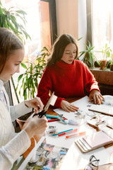 Two friends collaborate on a fun art project surrounded by greenery. They cut and organize colorful materials, enjoying each other's company as sunlight streams through the window.
