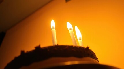 Chocolate cake with three lit candles on top warmly lit