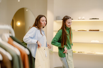 Two friends are trying on different pants in a bright, contemporary clothing store. They share smiles as they enjoy their shopping experience, surrounded by stylish apparel.
