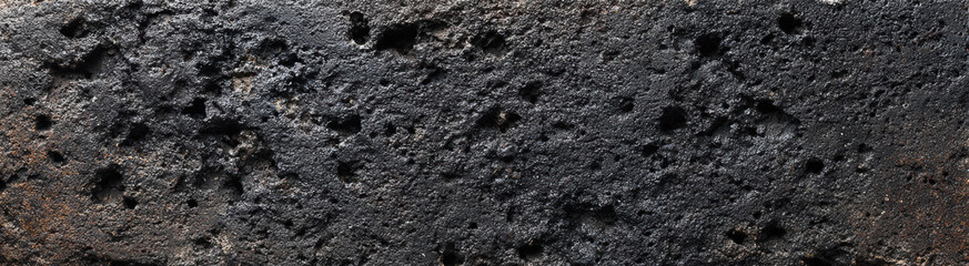 Dark porous texture of rough black stone surface background showing natural detail and grit pattern of hard rock material often found in volcanic terrain or charred surfaces evoking heavy mood