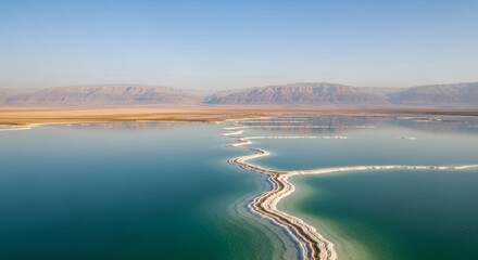 A winding salt formation snakes across the turquoise waters of the Dead Sea, with barren mountains in the background.