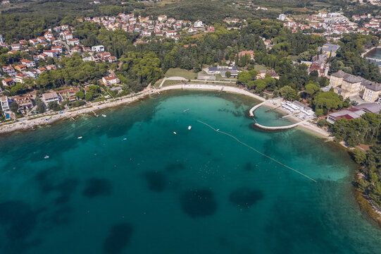 Aerial view of the turquoise waters gently lapping against the shore near a sandy beach and the coastline of Rovinj, Istria County, Croatia.