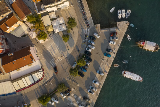 Aerial view of a harbor where cars line up along the pier and boats bob gently in the blue Adriatic waters, Rovinj, Istria County, Croatia.