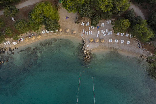 Aerial view of sun-kissed beach with rows of white loungers and straw umbrellas meeting the turquoise waters, Rovinj, Istria County, Croatia.