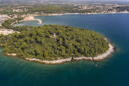 Aerial view of a lush, green island meeting the turquoise sea, with Punta Corrente in the heart of the island, contrasting with the mainland's sandy beach, Rovinj, Istria County, Croatia.