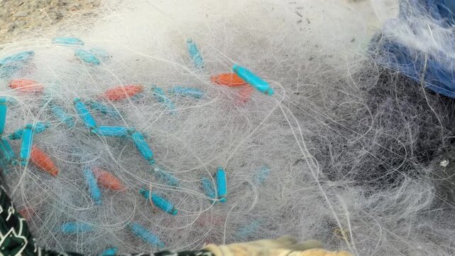 Fishermen hands untangle and spread fishing nets on the ground, thin lines and floats filling the frame as routine preparation unfolds before heading out to sea. Fishing preparation.