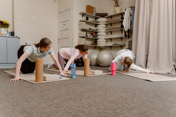 Three women engage in a yoga session in a bright studio. They focus on their poses using props, promoting relaxation and physical strength in a calming environment.