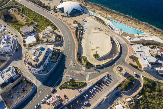 Aerial view of the vibrant roundabout near the shimmering coast and the distinctive dome-shaped structure, Bugibba, St. Paul's Bay, Malta.