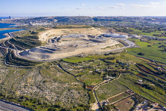 Aerial view of a vast quarry contrasting with the surrounding vibrant green fields and distant coastal town, Bugibba, St. Paul's Bay, Malta.