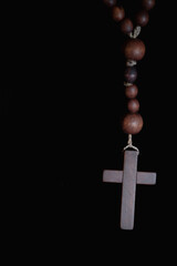 Wooden rosary with cross hanging in darkness, symbolizing faith, prayer, devotion, spirituality, repentance, hope, and silent inner reflection.