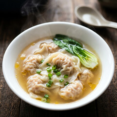 Steaming hot wonton soup with bok choy and scallions in a white bowl.