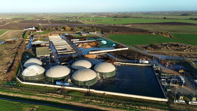 Aerial view of a biogas plant with its distinctive domed digesters contrasting against the surrounding green fields, Wisbech, England, United Kingdom.