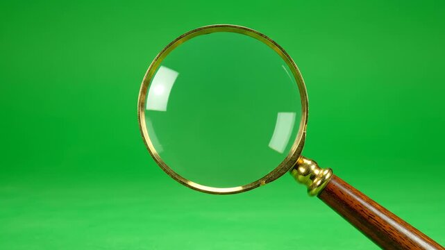 Isolated studio shot of a classic wooden-handled magnifying glass rotating slowly against a pure green screen backdrop, ready for compositing search footage alpha, glass, up