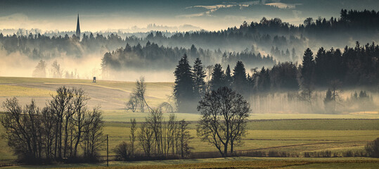 Mystische Nebellandschaft mit Kirchturm und Baum-Silhouetten im morgendlichen Dunst in Bayern © florentina.p