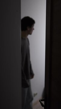 Man hesitating and pacing behind open door, thinking and unable to decide, quiet moment of doubt and inner conflict. Vertical video
