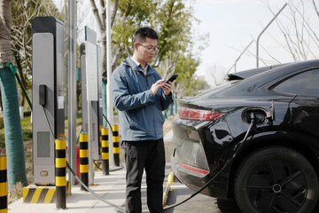 asian Man uses phone at EV charging spot
