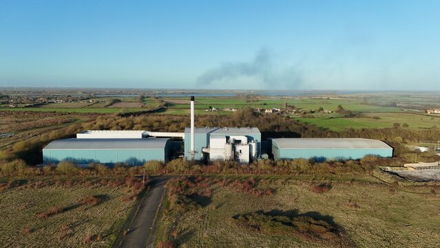 Aerial view of an industrial building with a tall chimney contrasts against the flat landscape under a clear sky, Ely, England, United Kingdom.