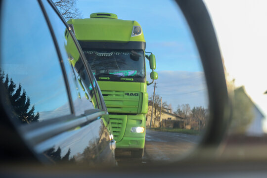 Kaliniv, Ukraine - December 10, 2025: ​A bright green DAF truck is reflected in a car's side mirror while driving on a road during a sunny day.