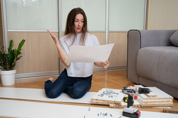 woman sitting among furniture parts on the floor looks at the assembly instructions with confused expression and questioning hand gesture