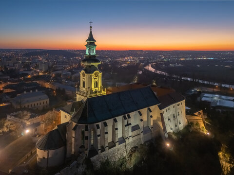 Aerial view of Nitra Castle bathed in soft light against the backdrop of a twilight sky, its illuminated tower a beacon in the serene landscape., Nitra, Nitriansky kraj, Slovakia.