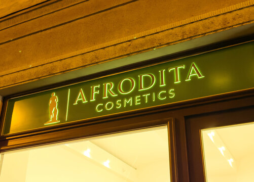 Illuminated storefront of Afrodita Cosmetics, showcasing vibrant green signage and elegant design, inviting customers to explore beauty products in a charming urban setting