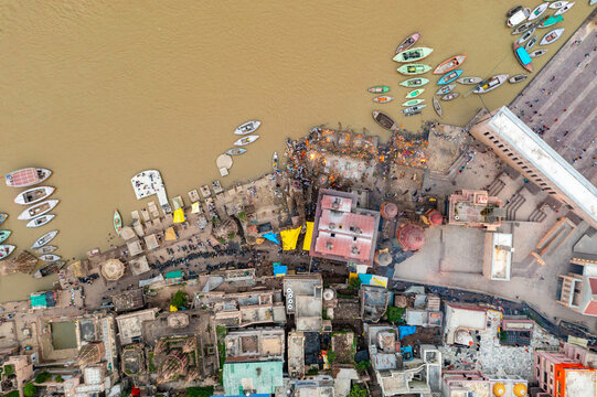 Aerial view of ochre river embraces ghats lined with boats and buildings, where life and death intertwine in a sacred dance, Varanasi, Uttar Pradesh, India.