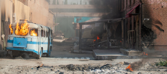 horizontal background with an explosion on a street with damaged houses and a burning bus © serhii