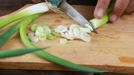 close up female hand holding knife, cutting fresh leek on chopping board