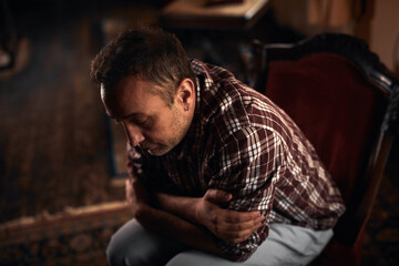 Man with headache, depression, sadness and loneliness sitting on a chair at home.