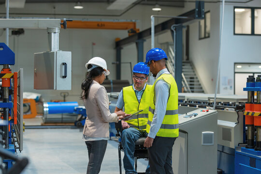 Factory woman CEO touring with an employee the production line, where another worker with a disability expertly completing his tasks.