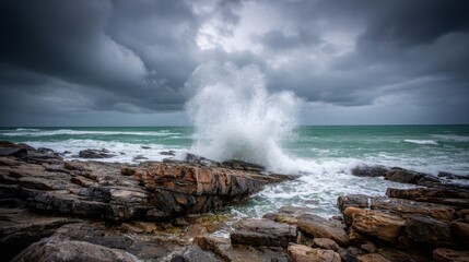 Powerful ocean wave powerfully crashes against rugged rocky coastline under dramatic stormy clouds, capturing elemental force and wild nature.