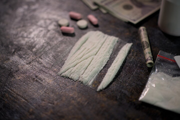 Illicit white powder lines and various pills laid out on a dark, textured surface near currency.