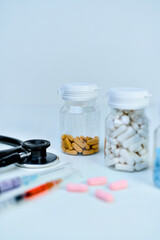 Medical essentials featuring an examination stethoscope, various prescription pill bottles, and colorful syringes on a white surface.