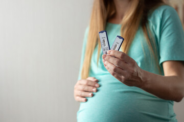 Pregnant woman holding rapid tests for hepatitis and gently touching her belly. Negative tests for hepatitis. Closeup