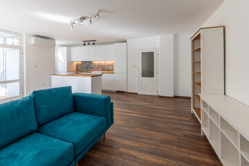 Modern open-plan living room and kitchen interior. Bright, spacious apartment with a teal sofa,...